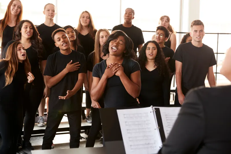 Young singers rehearsing together in a choir, sheet music on a stand in the foreground