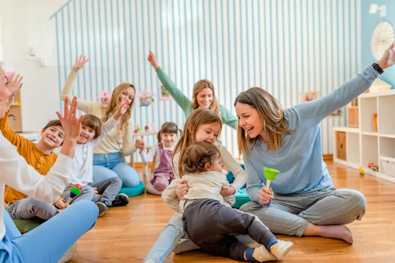 Caregivers and toddlers sitting in a circle with shakers and bells during an early-childhood music class