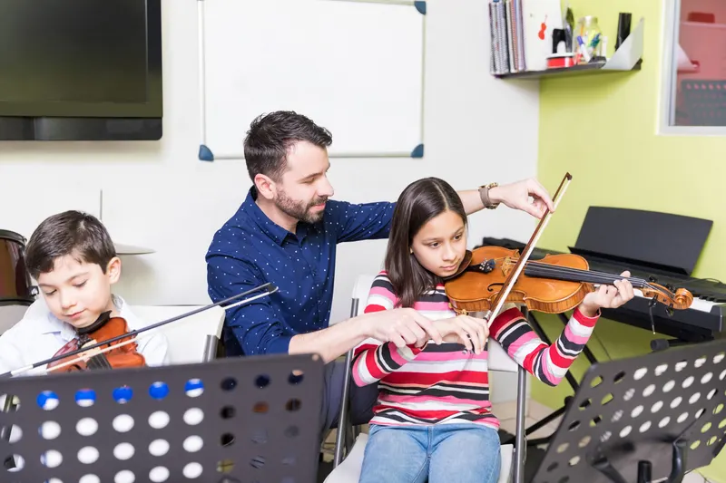 Violin teacher adjusting a young student's bow arm during a group string lesson