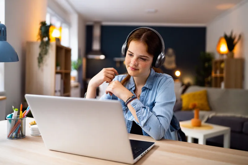 A teenager with headphones in an online tutoring session at a home desk, laptop open