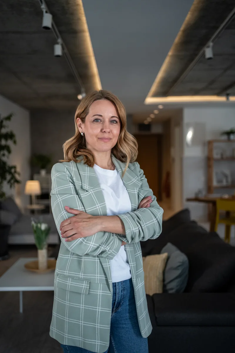 Standing portrait of a woman in a sage checked blazer with arms crossed in a warm modern loft space