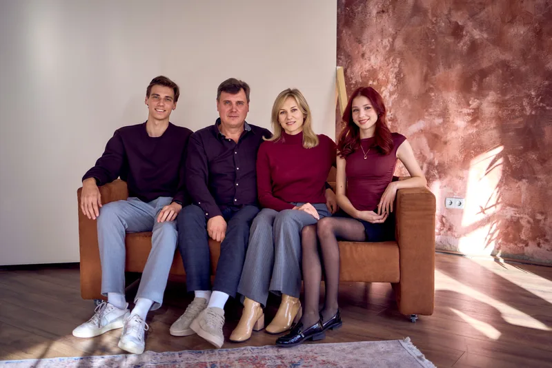 Parents and their two adult children seated together on a sofa at home — the two generations a family plan has to serve