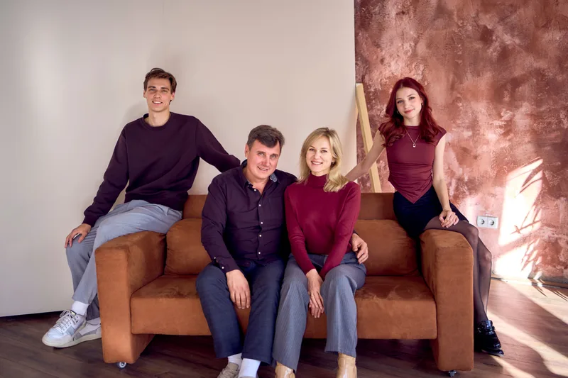 A family of four gathered on and around a sofa, parents seated between their adult son and daughter