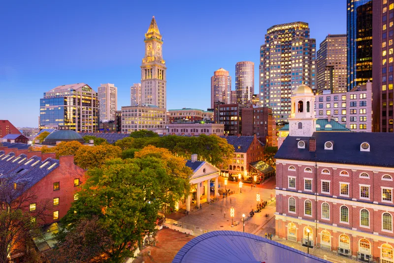 Boston's Custom House Tower and financial district at dusk, seen over the trees and brick rooftops near Faneuil Hall