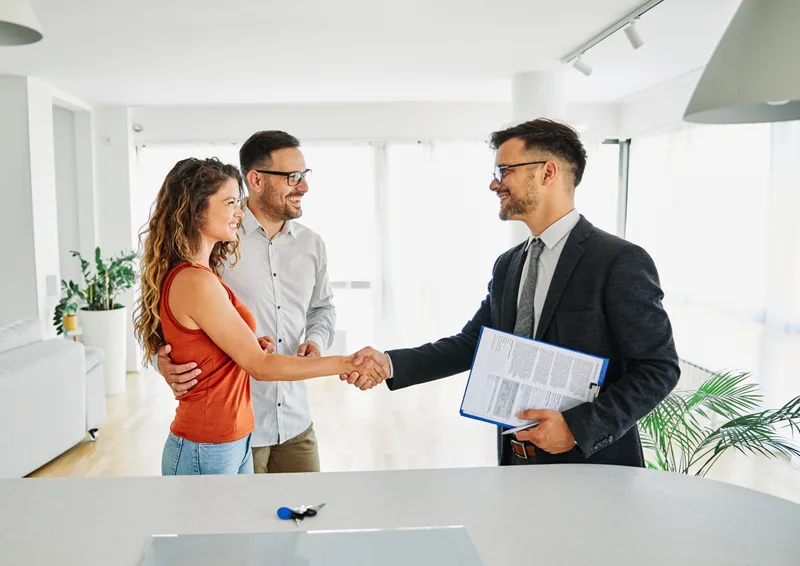 A Crescent Loans funding advisor shaking hands with two small-business owners across a desk, loan documents in hand