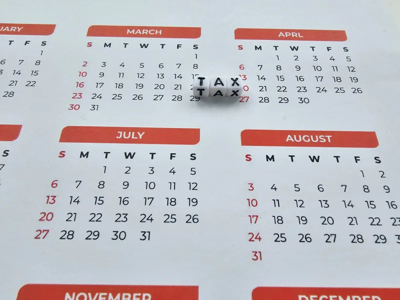 A printed wall calendar with letter blocks spelling TAX resting on one of the spring dates