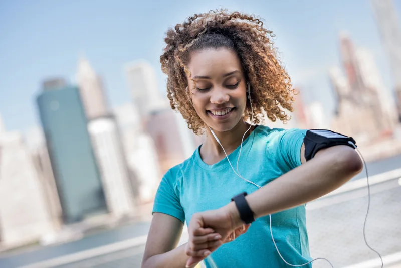 Priya checking the training plan on her sports watch mid-run, city skyline behind her