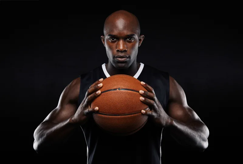 Marcus holding a basketball at chest height, photographed in dramatic low light before an evening league game