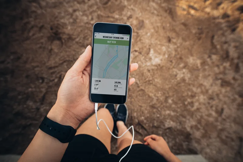 A lifter's hand holding a phone with the day's training session open, mid-workout outdoors