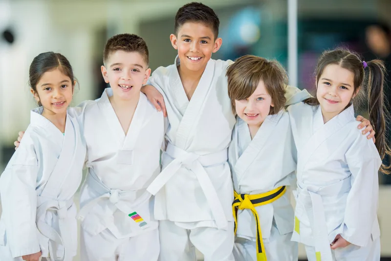 Five smiling kids in white karate gis standing arm in arm on the mat after class