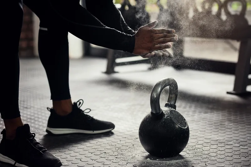 Lifter bending down and dusting chalk from their hands over a cast-iron kettlebell on a rubber gym floor