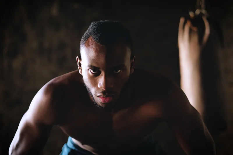 Boxer looking straight into the camera between rounds, a heavy bag hanging out of focus behind him