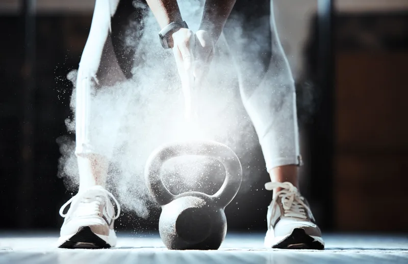 Cloud of lifting chalk drifting over a kettlebell between an athlete's feet on a gym floor