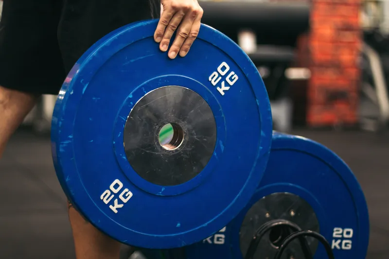 Hand resting on a stack of blue 20-kilogram competition bumper plates