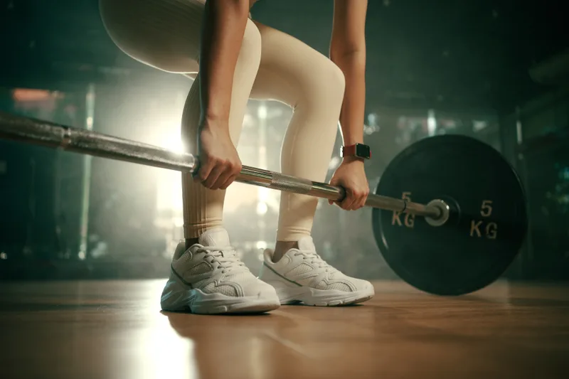 Lifter gripping a loaded barbell at the top of a deadlift setup on a hardwood platform under moody green-tinted light