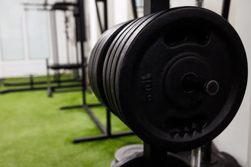 Stack of black iron plates racked on a bar beside a strip of green turf