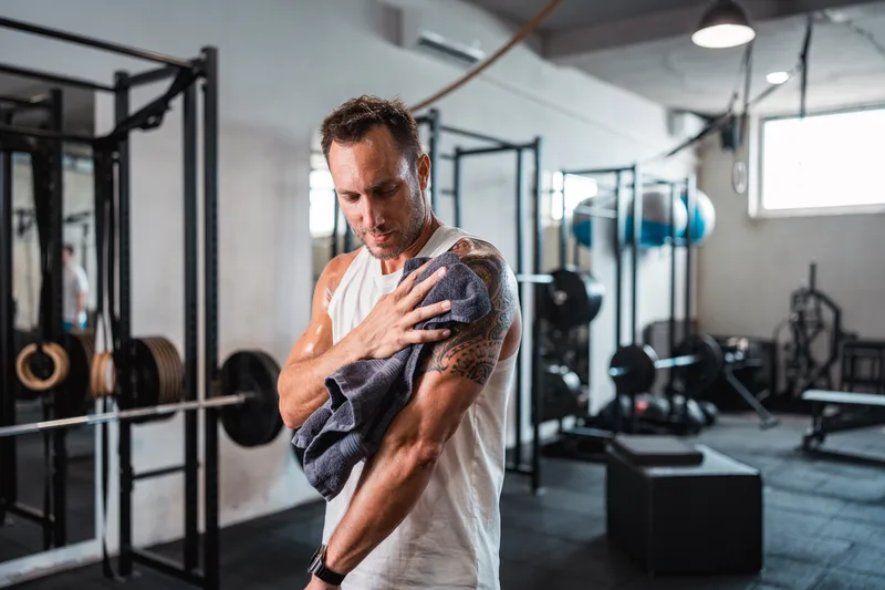 Member toweling off his shoulder between sets in an industrial gym full of racks