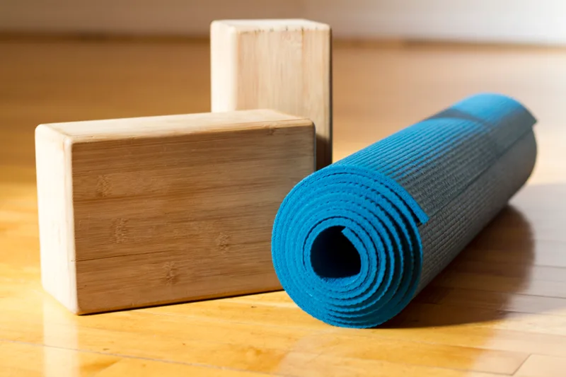 Two wooden yoga blocks beside a rolled blue mat on a wooden floor