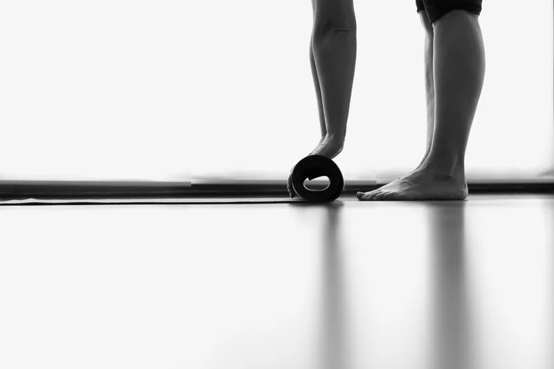 Bare feet beside a half-rolled black mat on a sunlit studio floor, photographed in black and white