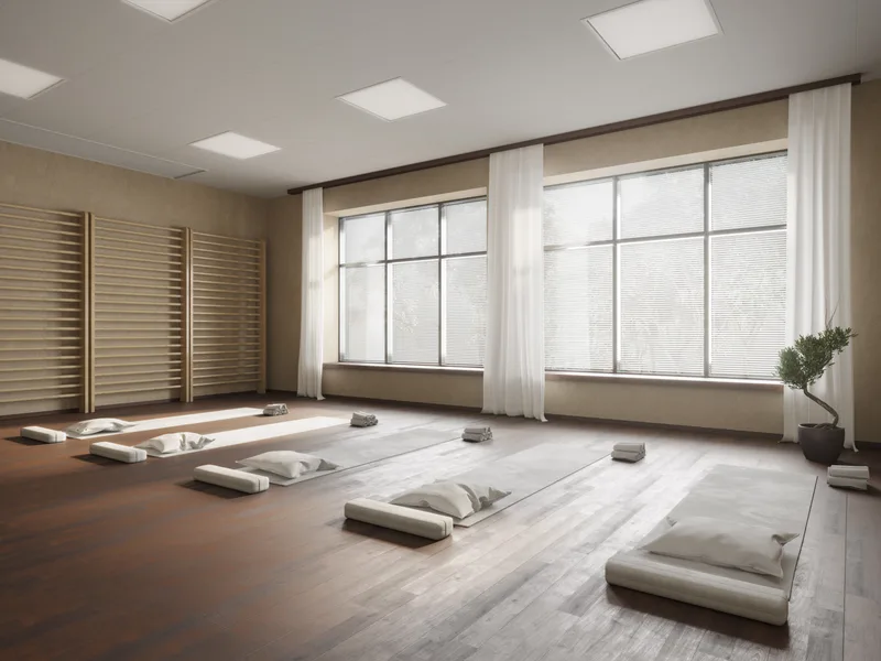 Calm retreat practice room with floor cushions arranged in rows beneath tall curtained windows