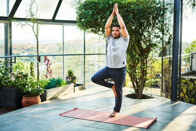 Guest balancing in tree pose on a plant-filled terrace in golden morning light