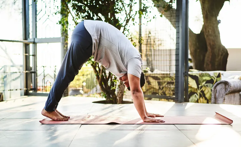 Guest stretching through downward dog on a sunlit patio surrounded by greenery