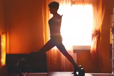 Silhouette of a student holding a deep lunge on a reformer against a glowing curtained window