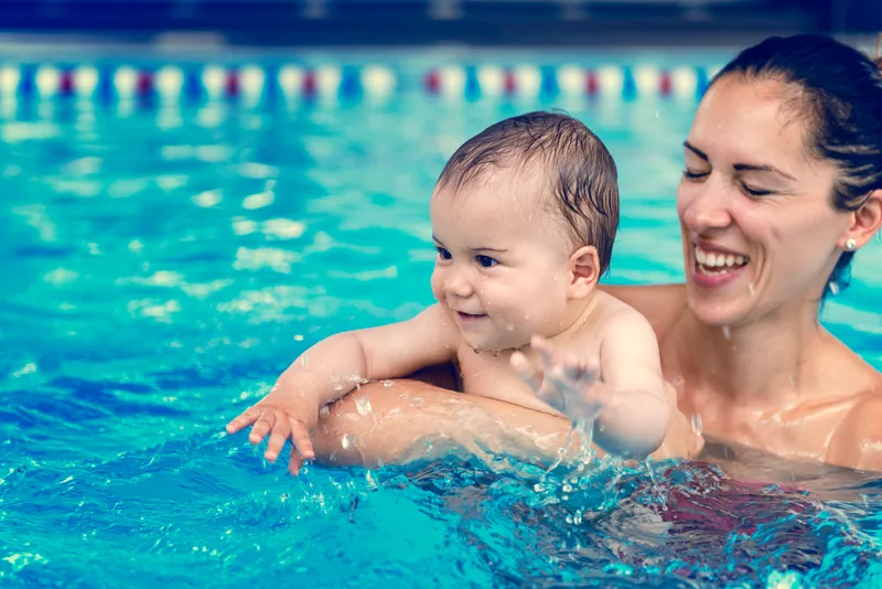 Smiling mother holding her baby at the surface of a pool with lane markers behind them