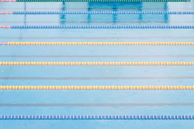 Overhead view of calm pool water crossed by yellow and blue lane ropes