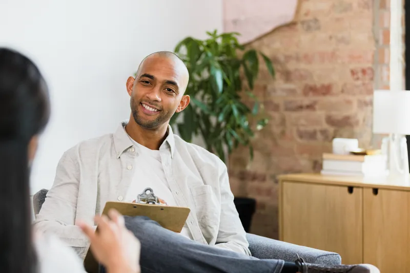 A counselor with a clipboard listening and smiling during a one-to-one session