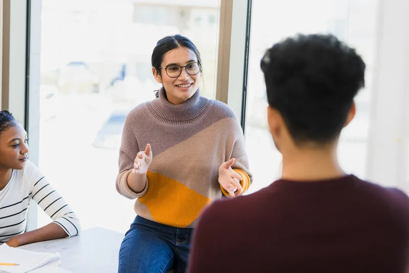 A counselor in a sweater talking with a small group sitting together in a bright room
