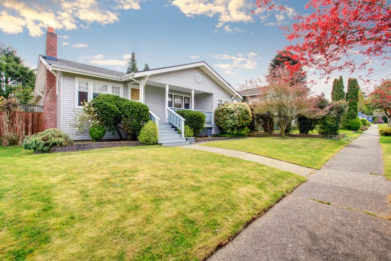 A beige house with a covered front porch, a lawn and a garden path