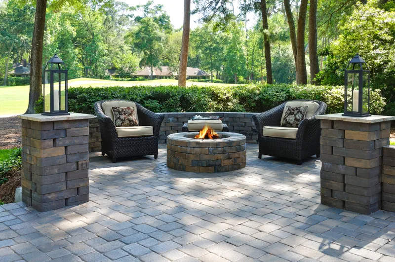 A stone patio with armchairs around a fire pit, surrounded by trees
