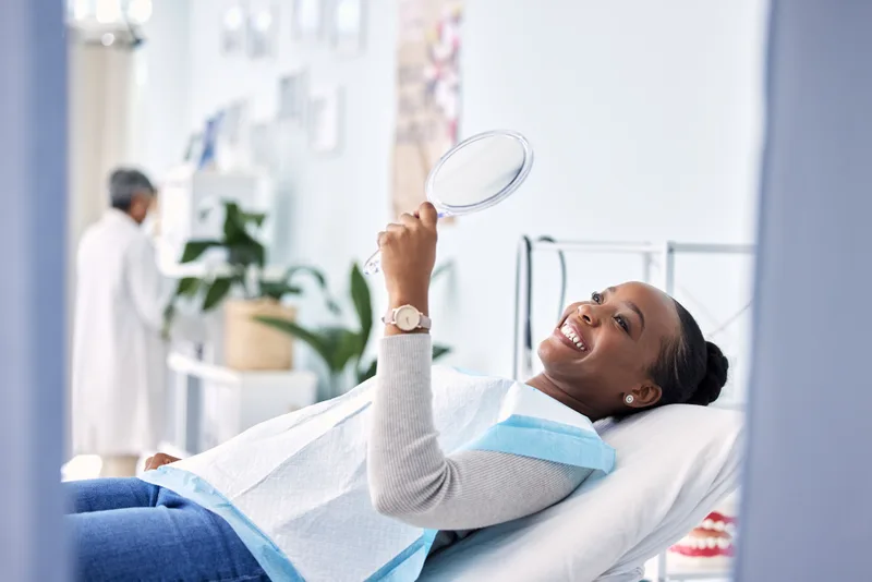 Patient reclining in a dental chair, smiling as she looks into a hand mirror