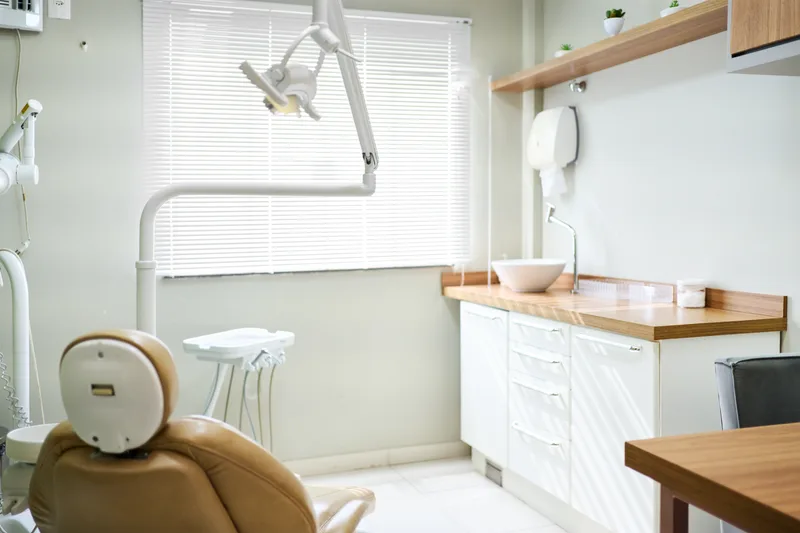 Calm treatment room with a cream dental chair, warm wood counter and daylight from a large window