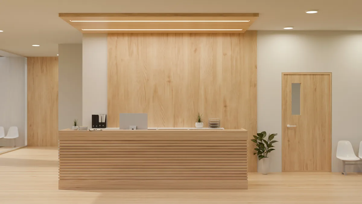 Atrium's light-oak reception desk under a warm ceiling light, with chairs that rarely get used for waiting