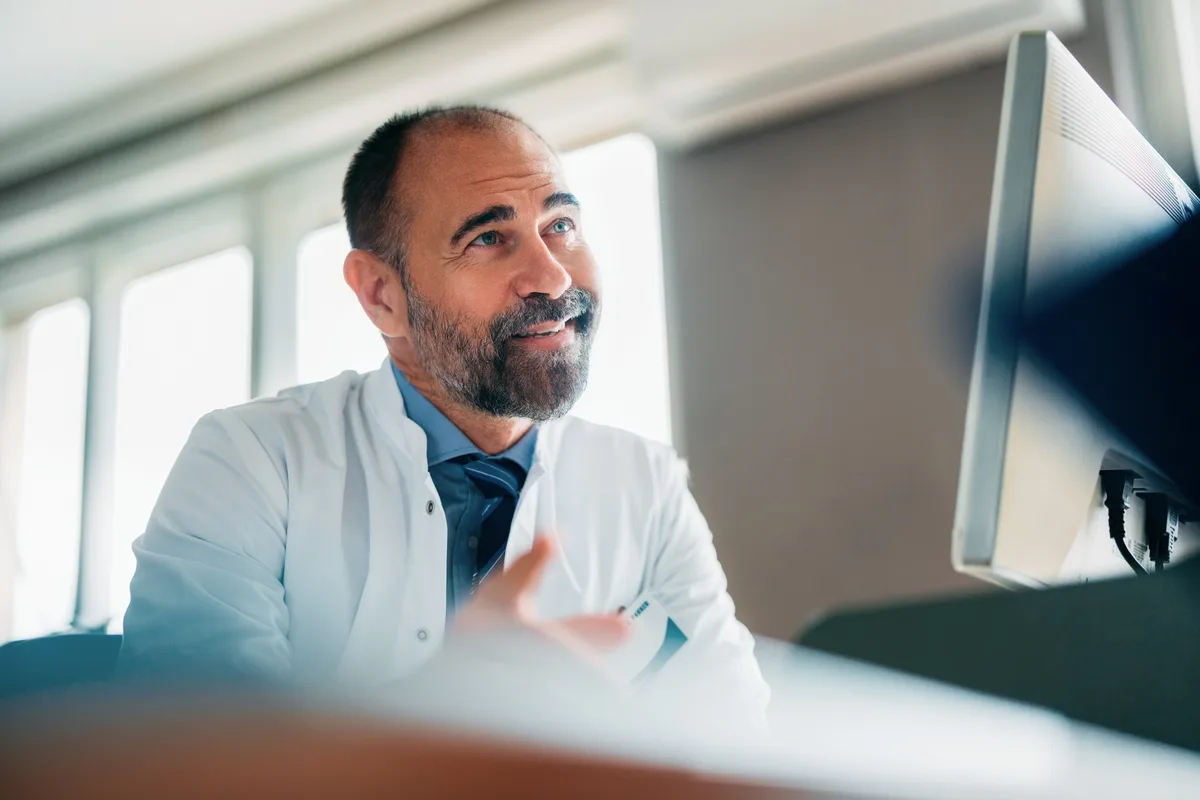 An Atrium physician at his desk, smiling as he replies to a member's message on screen
