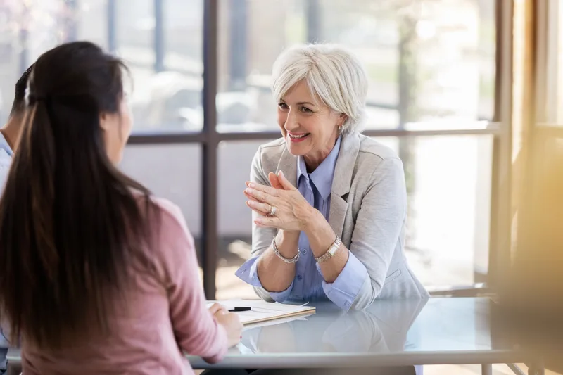 Silver-haired therapist smiling warmly as she talks with a couple across a sunlit table