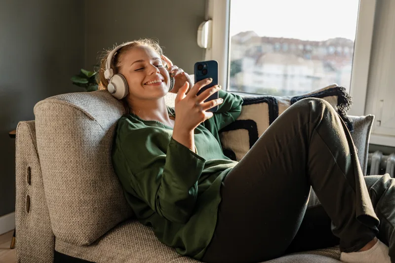 Smiling woman relaxing on a couch with headphones, following a session on her phone