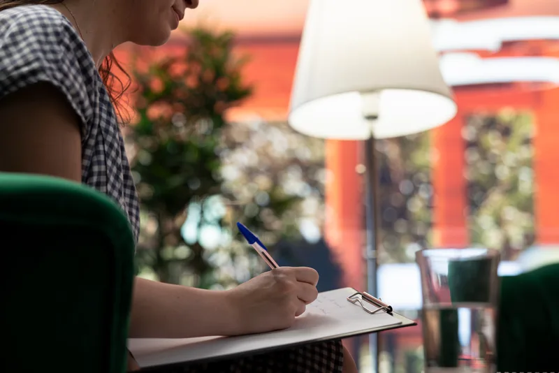 Close-up of a therapist writing intake notes on a clipboard beside a warm lamp