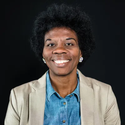 Dr. Maya Okafor, a smiling psychologist in a tan blazer and denim shirt