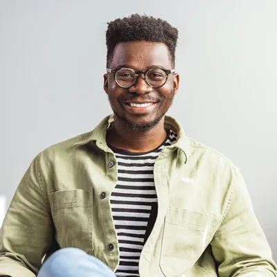 Marcus Adeyemi, a warmly smiling therapist in glasses and a sage overshirt