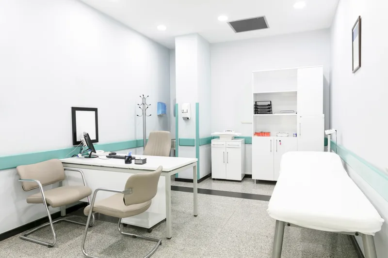 A quiet, empty consult room with a desk, two chairs and an exam couch, ready for the next private visit