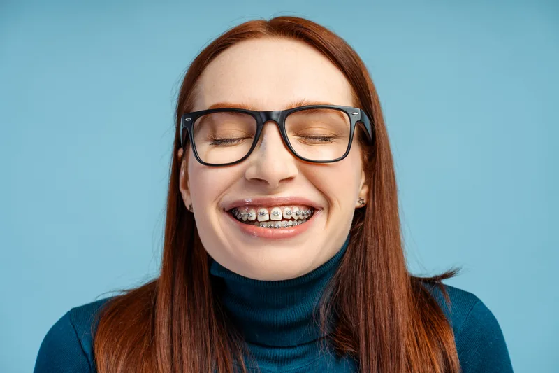 Adult woman with glasses and braces laughing with her eyes closed