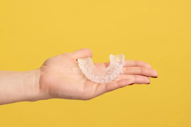 Open hand holding a clear aligner tray against a sunny yellow background