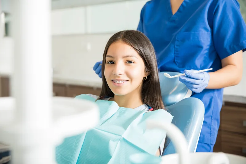 Smiling teenage girl with braces in the chair with an orthodontic assistant behind her