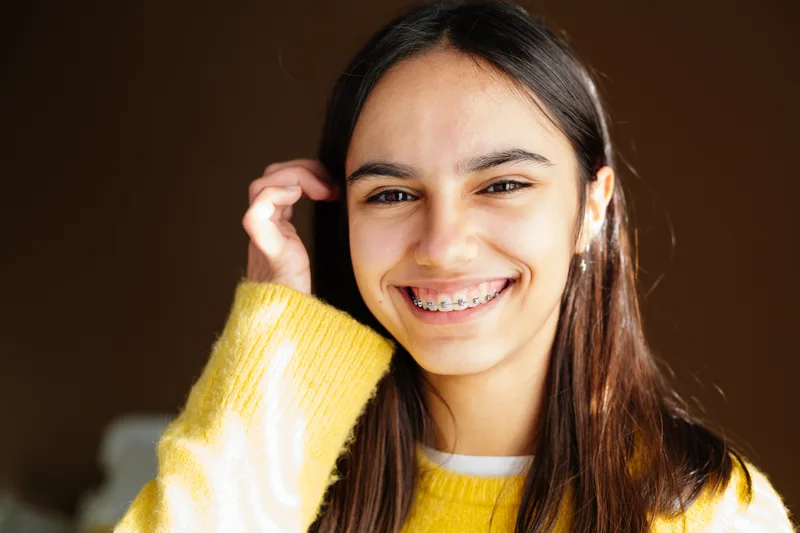 Smiling teenage girl in a yellow sweater showing her braces