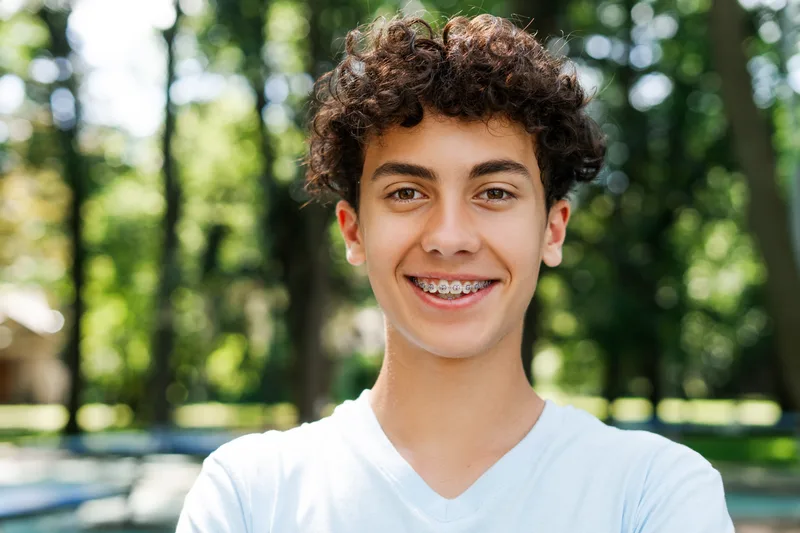 Teenage boy with braces smiling outdoors in a park