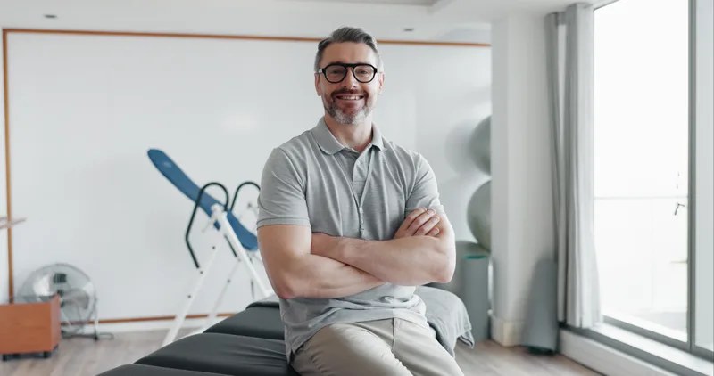 Dr. Daniel Reyes, smiling with arms crossed, sitting on a treatment table in the clinic