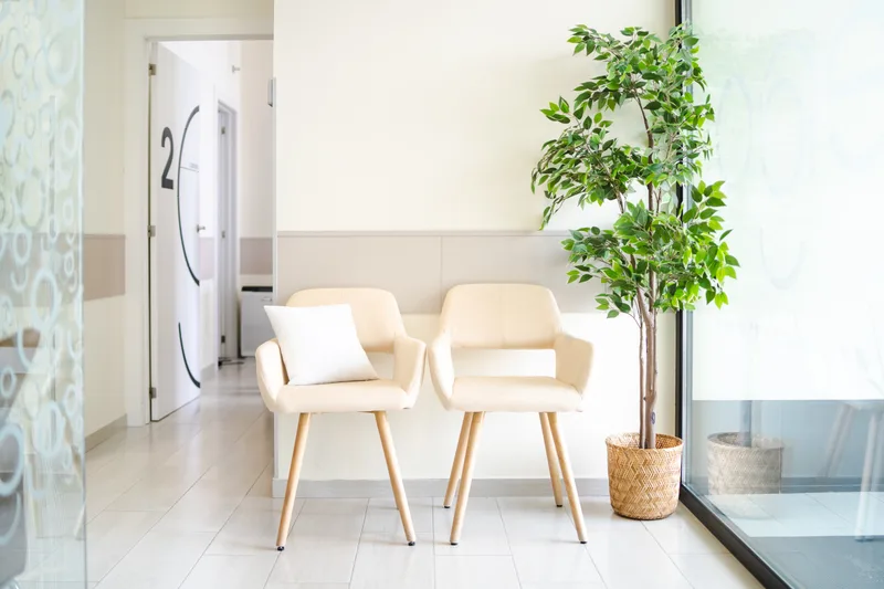 A bright, quiet clinic waiting area with two cream chairs and a plant